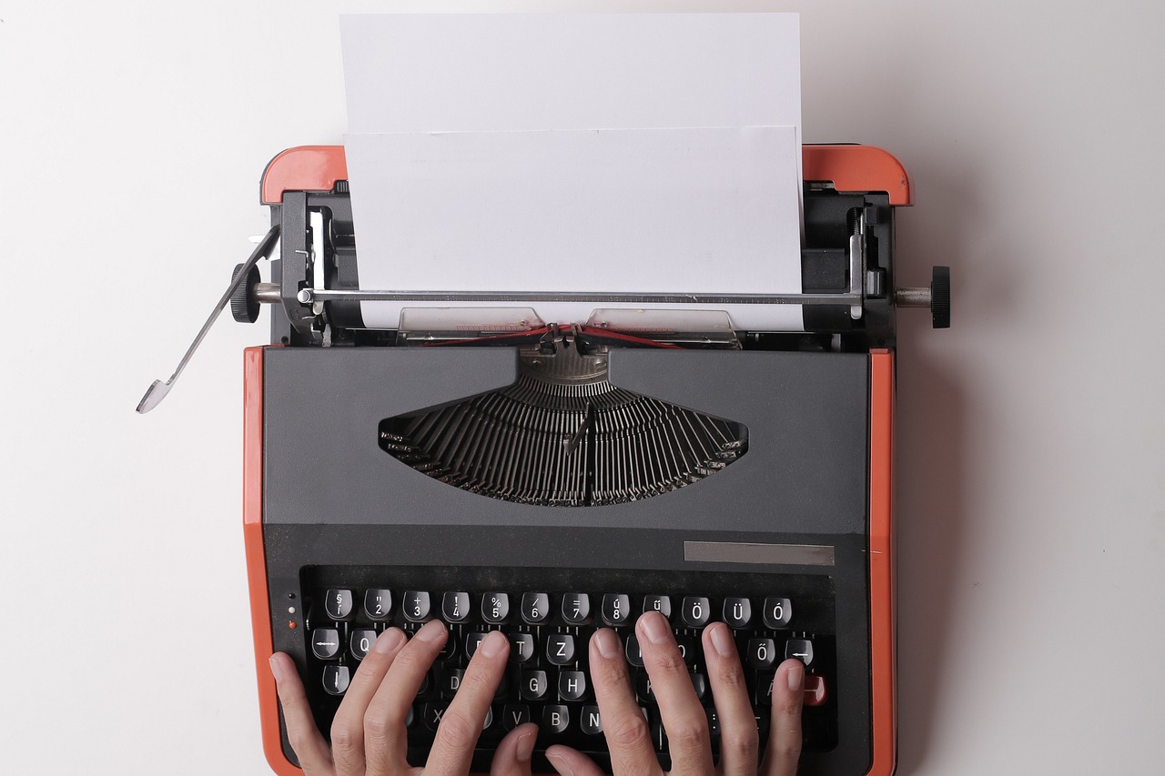 Hands typing a draft on a vintage typewriter