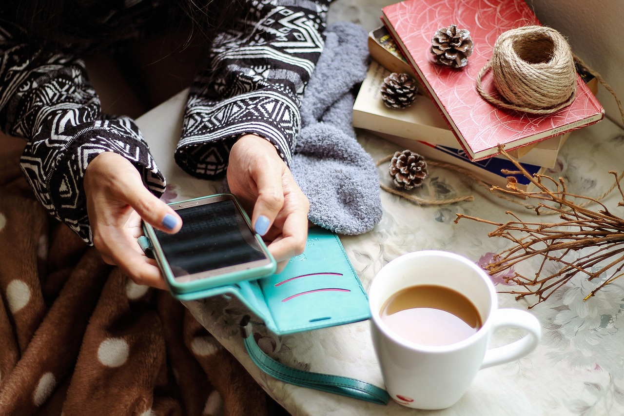 Young woman checking social media on her smartphone beside a cup of coffee